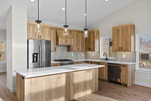 Kitchen with high quality appliances, pendant lighting, light wood-type flooring, decorative backsplash, and vaulted ceiling