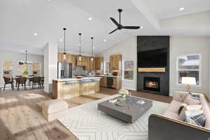 Living room with a premium fireplace, hanging lights, light wood-type flooring, a ceiling fan, and vaulted ceiling