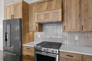 Kitchen with stainless steel appliances, tasteful backsplash, range hood, and light wood finish cabinetry