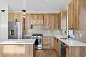 Kitchen featuring stainless steel appliances, light wood finish cabinetry, light stone counters, pendant lighting, and tasteful backsplash