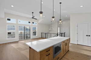 Kitchen with light wood-type flooring, ceiling fan, hanging light fixtures, stainless steel microwave, and lofted ceiling