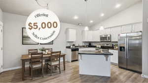 Open-concept kitchen and dining area featuring vaulted ceilings, wood-finish flooring, white cabinetry, and stainless steel appliances