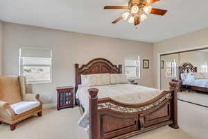 Primary bedroom with light carpet, a closet, and a ceiling fan