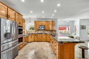 Kitchen with stainless steel appliances, dark stone countertops, a peninsula, a kitchen breakfast bar, and hanging light fixtures