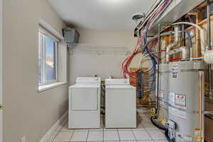 Laundry room with strapped water heater, washer and dryer, and light tile patterned floors