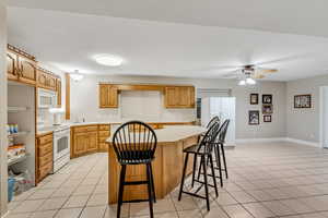 Kitchen featuring light countertops, a breakfast bar area, white appliances, a kitchen island, and a ceiling fan