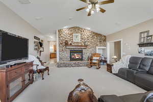 Carpeted living room featuring ceiling fan and a stone fireplace