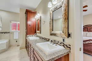 Primary full bath featuring double vanity, connected bathroom, a ceiling fan, and decorative backsplash