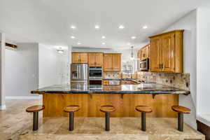 Kitchen with wood finish cabinets, dark stone counters, a peninsula, stainless steel appliances, and tasteful backsplash