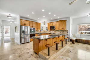 Kitchen with wood finish cabinetry, a breakfast bar area, stainless steel appliances, tasteful backsplash, and dark stone counters