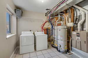 Laundry area featuring strapped water heater, washer and dryer, heating unit, and light tile patterned floors