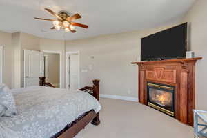 Primary bedroom featuring light carpet, a ceiling fan, and a glass covered fireplace