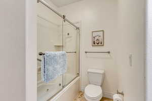 Full bathroom with toilet and bath / shower combo with glass door