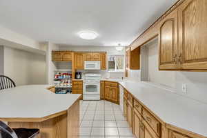 Kitchen featuring light countertops, white appliances, a breakfast bar area, and wood finish cabinetry