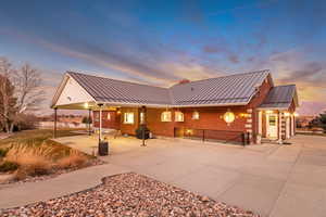 Back of property at dusk with brick siding, a standing seam roof, a chimney, and a patio area
