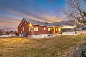 Back of house at dusk featuring a standing seam roof, brick siding, a patio area, a chimney, and a mountain view
