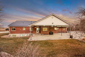 Back of house with brick siding, a patio, a lawn, a metal roof, and entry steps