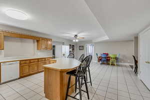 Kitchen with light countertops, light tile patterned floors, white appliances, a center island, and a breakfast bar