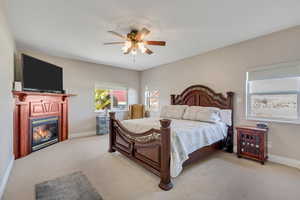 Primary bedroom with a glass covered fireplace, carpet flooring, and ceiling fan