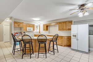 Kitchen featuring white appliances, light countertops, a kitchen breakfast bar, a center island, and light tile patterned flooring