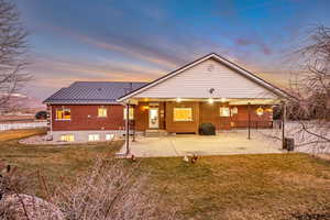 Back of house at dusk featuring a yard, a patio, brick siding, and entry steps