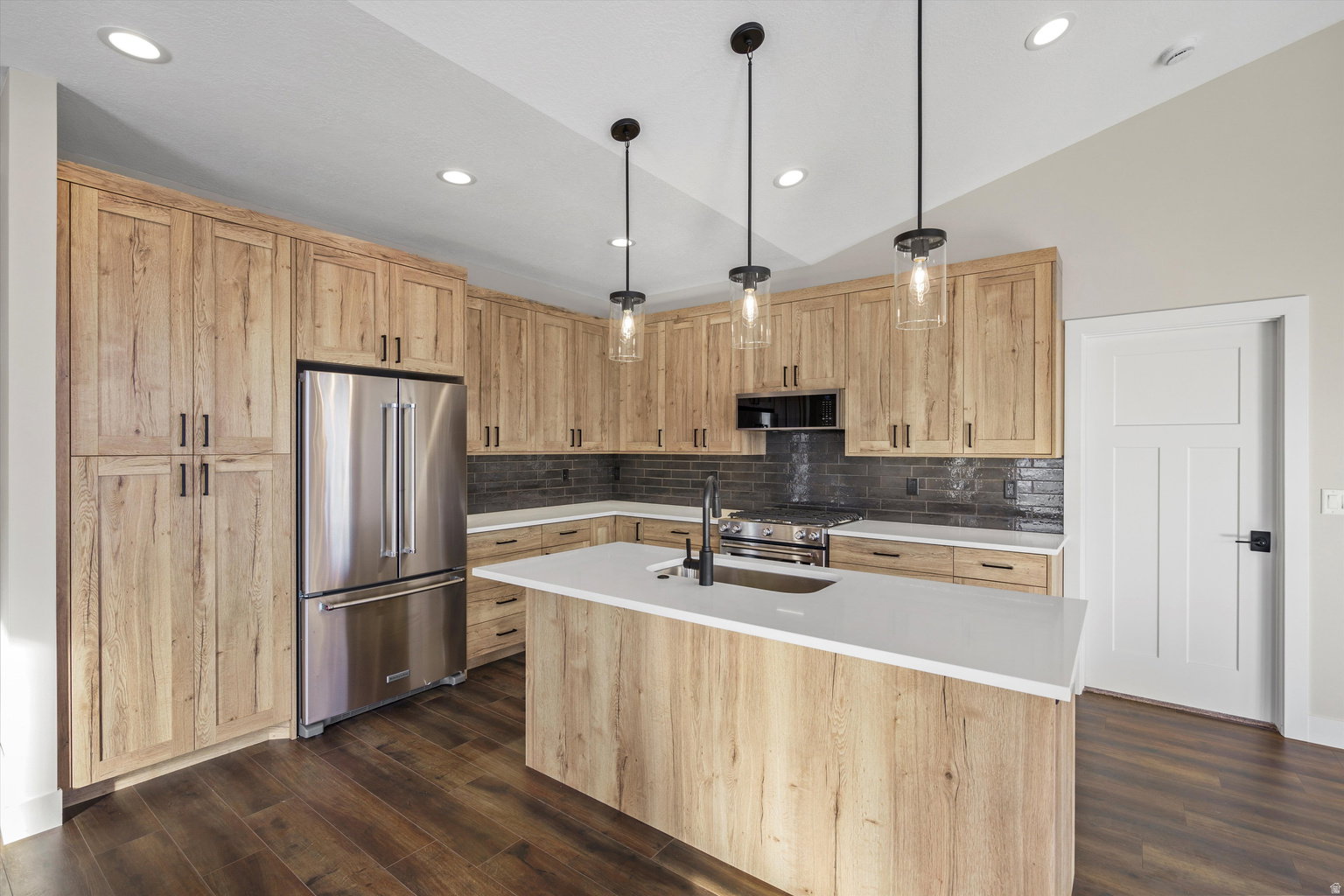 Kitchen featuring light wood finish cabinets, high quality appliances, a kitchen island with sink, dark wood-style floors, and decorative backsplash