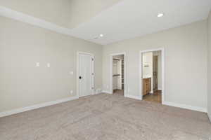 Unfurnished bedroom with recessed lighting, a walk in closet, light carpet, and ensuite bath