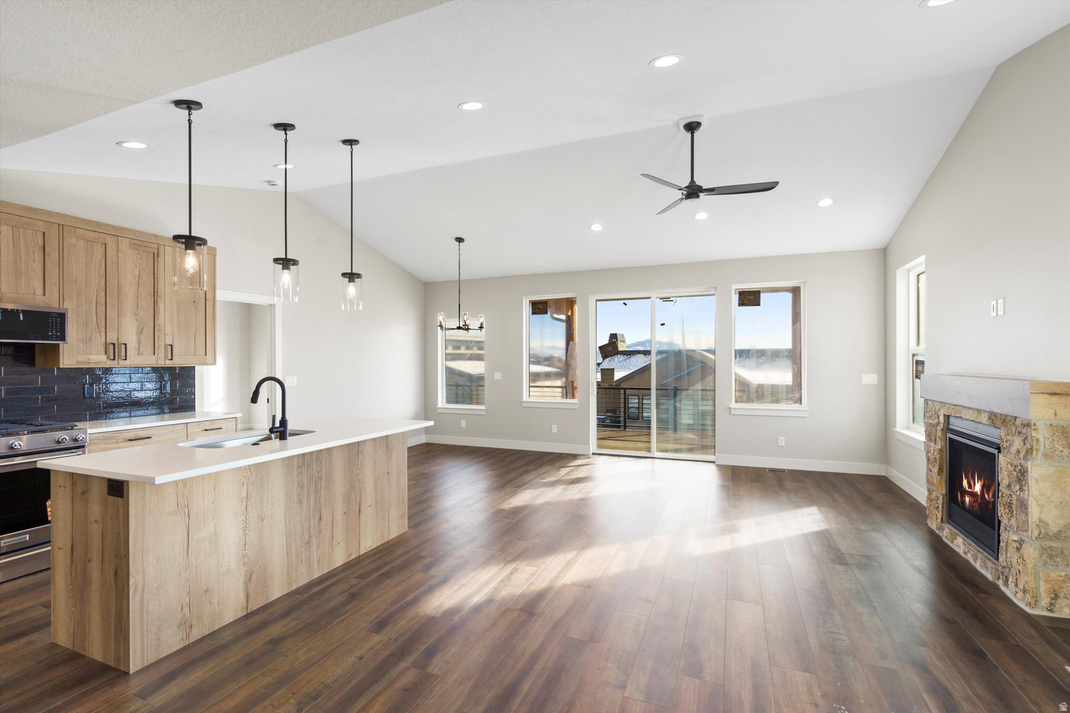 Kitchen featuring a stone fireplace, light wood finish cabinetry, vaulted ceiling, open floor plan, and gas range