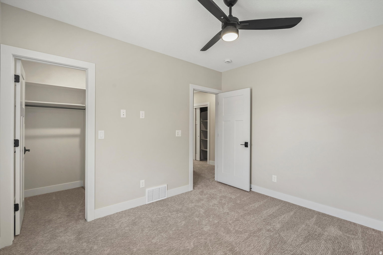 Unfurnished bedroom with a spacious closet, light carpet, and a ceiling fan
