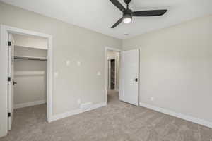 Unfurnished bedroom with a spacious closet, light carpet, and a ceiling fan