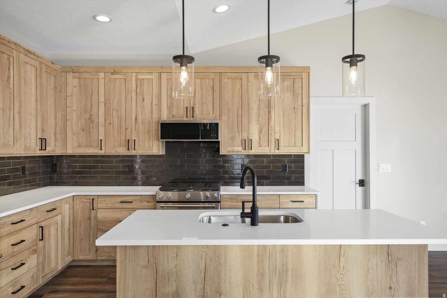 Kitchen with light wood finish cabinetry, stainless steel appliances, pendant lighting, dark wood finished floors, and lofted ceiling