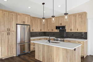 Kitchen with light wood finish cabinets, stainless steel appliances, a center island with sink, and dark wood-style floors