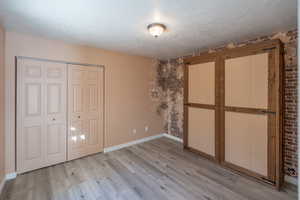Unfurnished bedroom with brick wall, a closet, light wood-style floors, and a textured ceiling