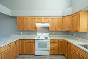 Kitchen with white range with electric stovetop, light stone countertops, and light wood-style floors