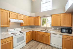 Kitchen featuring white appliances, light stone countertops, light wood-style floors, and a high ceiling