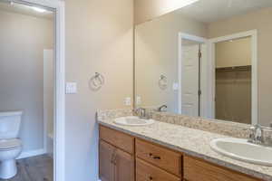 Full bathroom with double vanity, a walk in closet, and light wood finished floors
