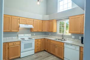 Kitchen with white appliances, light wood-type flooring, light stone countertops, and a high ceiling