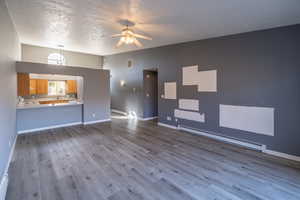 Unfurnished living room with a baseboard radiator, a ceiling fan, light wood finished floors, and a high textured ceiling