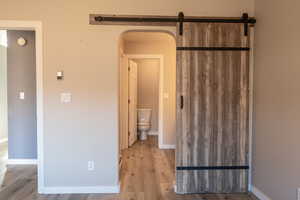 Unfurnished bedroom featuring arched walkways, a barn door, light wood finished floors, and ensuite bathroom