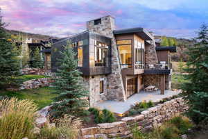 Rear view of property featuring stone siding, a balcony, a patio area, and outdoor dining area