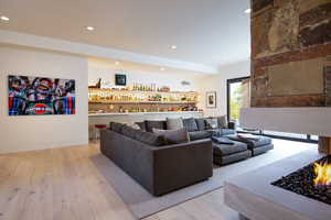 Living room with light wood-style floors, recessed lighting, and bar area