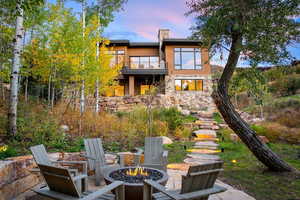 Back of property at dusk with a patio, a fire pit, a chimney, and a balcony