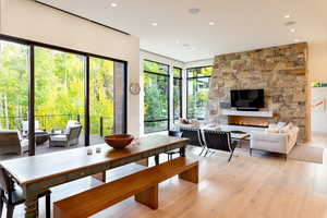 Dining room with light wood-style flooring, a stone fireplace, and recessed lighting