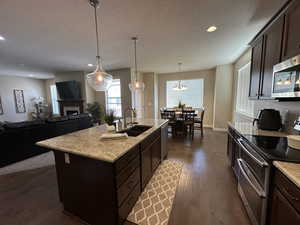 Kitchen with stainless steel appliances, dark wood finish cabinetry, a fireplace, dark wood-style floors, and a textured ceiling