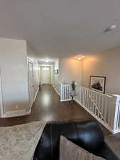 Corridor with dark wood-style flooring, an upstairs landing, and a textured ceiling