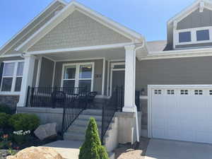 View of front of home featuring covered porch, a garage, concrete driveway, and stone siding