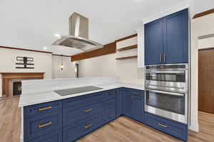 Kitchen with ornamental molding, blue cabinetry, open shelves, a tiled fireplace, and double oven