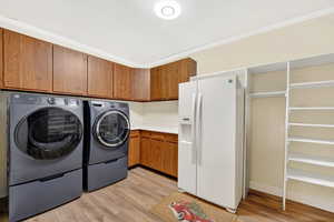 Laundry room featuring light wood-style flooring, washing machine and dryer, ornamental molding, and cabinet space