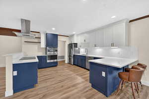 Kitchen featuring a peninsula, a breakfast bar, blue cabinetry, island range hood, and crown molding