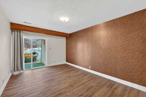 Empty room with wood finished floors, beamed ceiling, a textured ceiling, and an accent wall